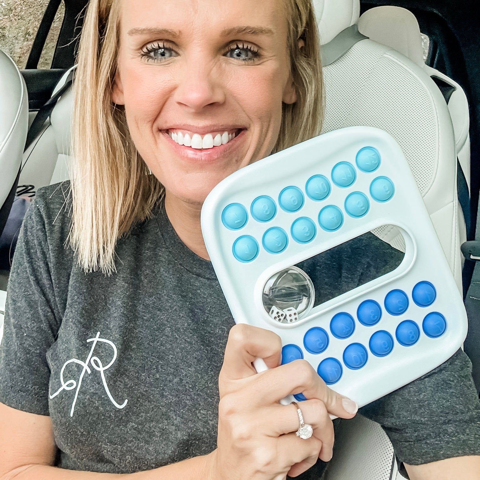 Woman holding a white device with blue buttons, sitting in a car.