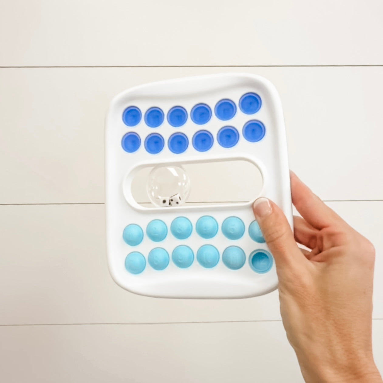 Hand holding a white game with blue silicone molds on a light wooden floor.
