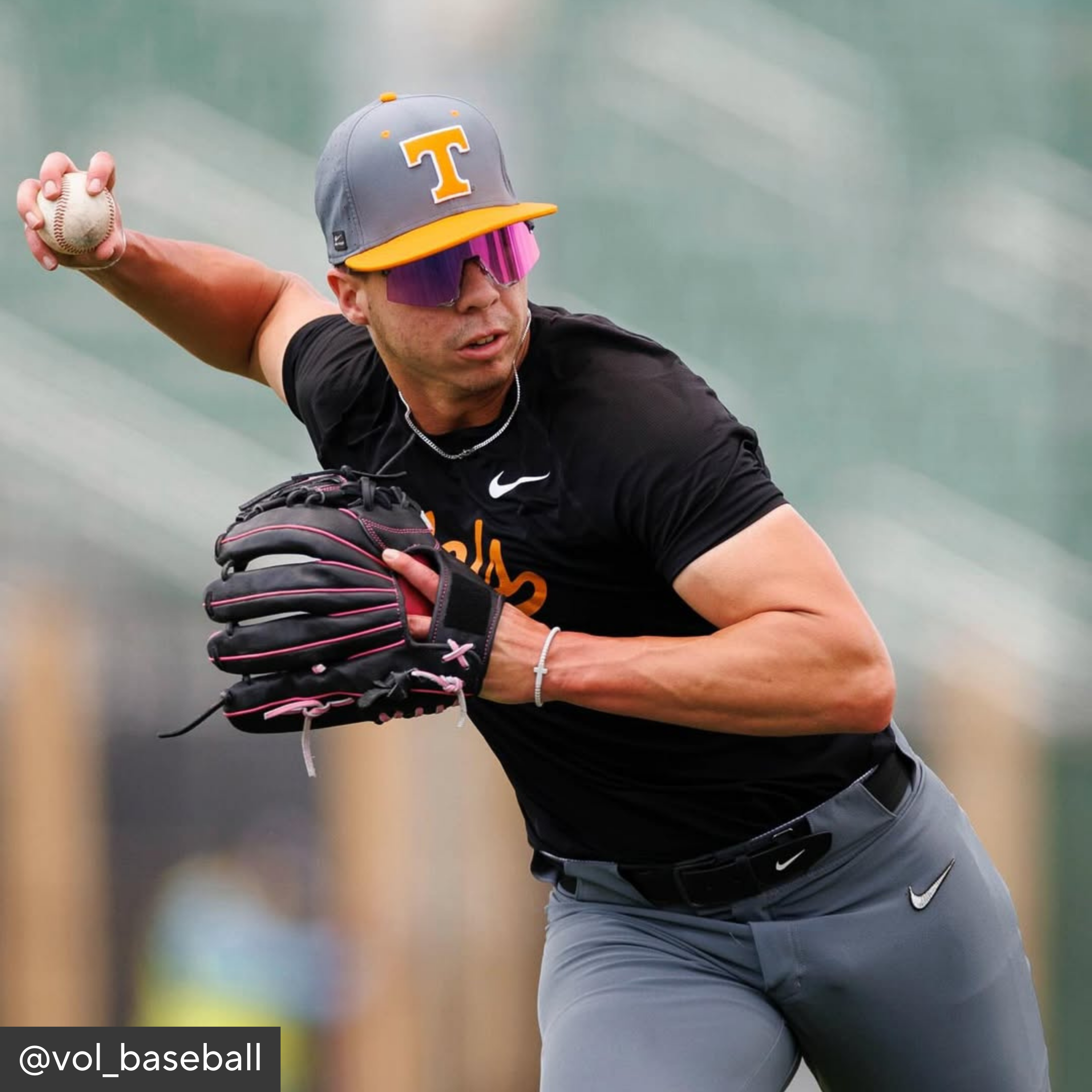 Baseball player in action wearing a black shirt, gray pants, and a gray cap with a yellow &