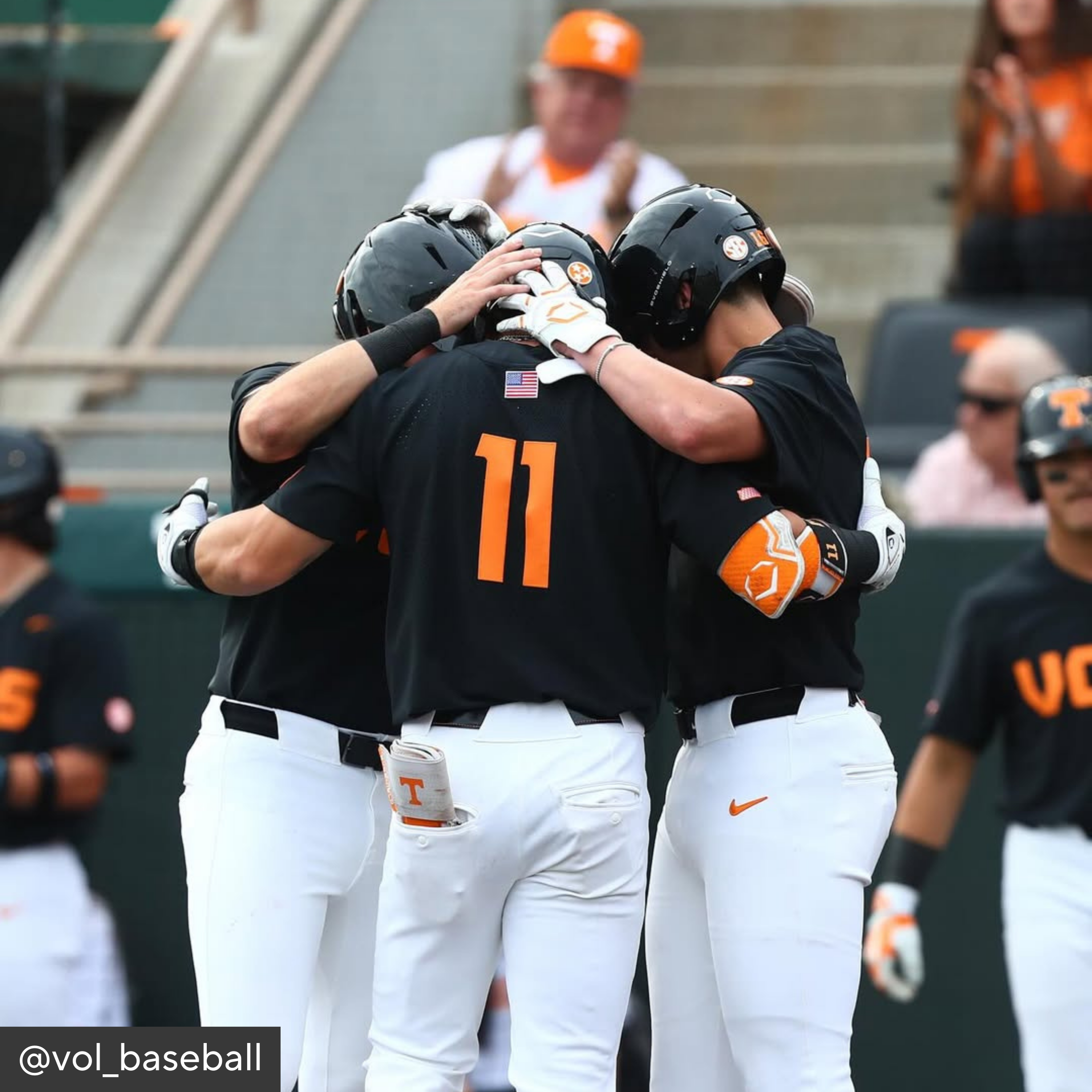 Baseball players in black jerseys with orange numbers hugging on a field