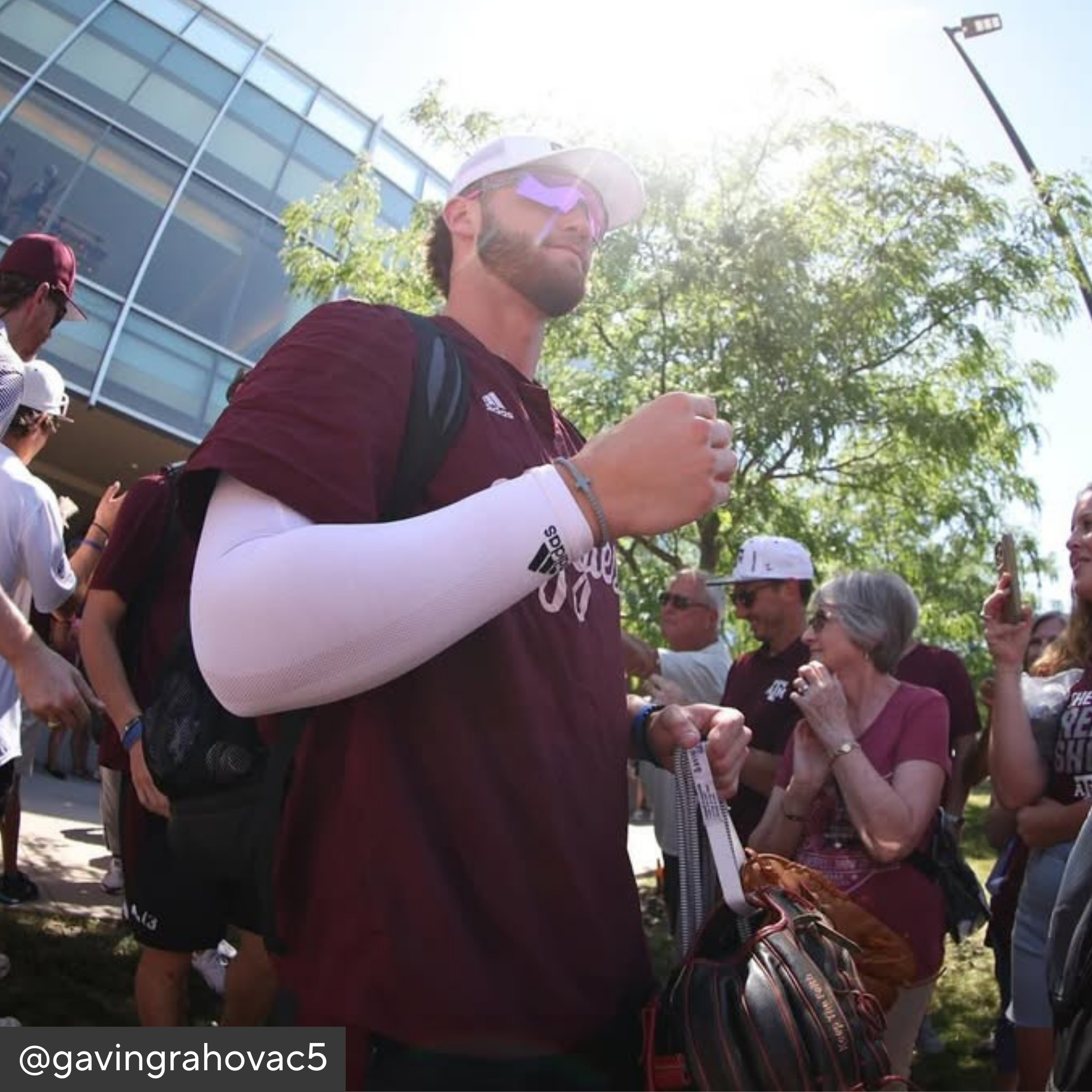 Man in maroon sports jersey with white sleeves interacting with people outdoors