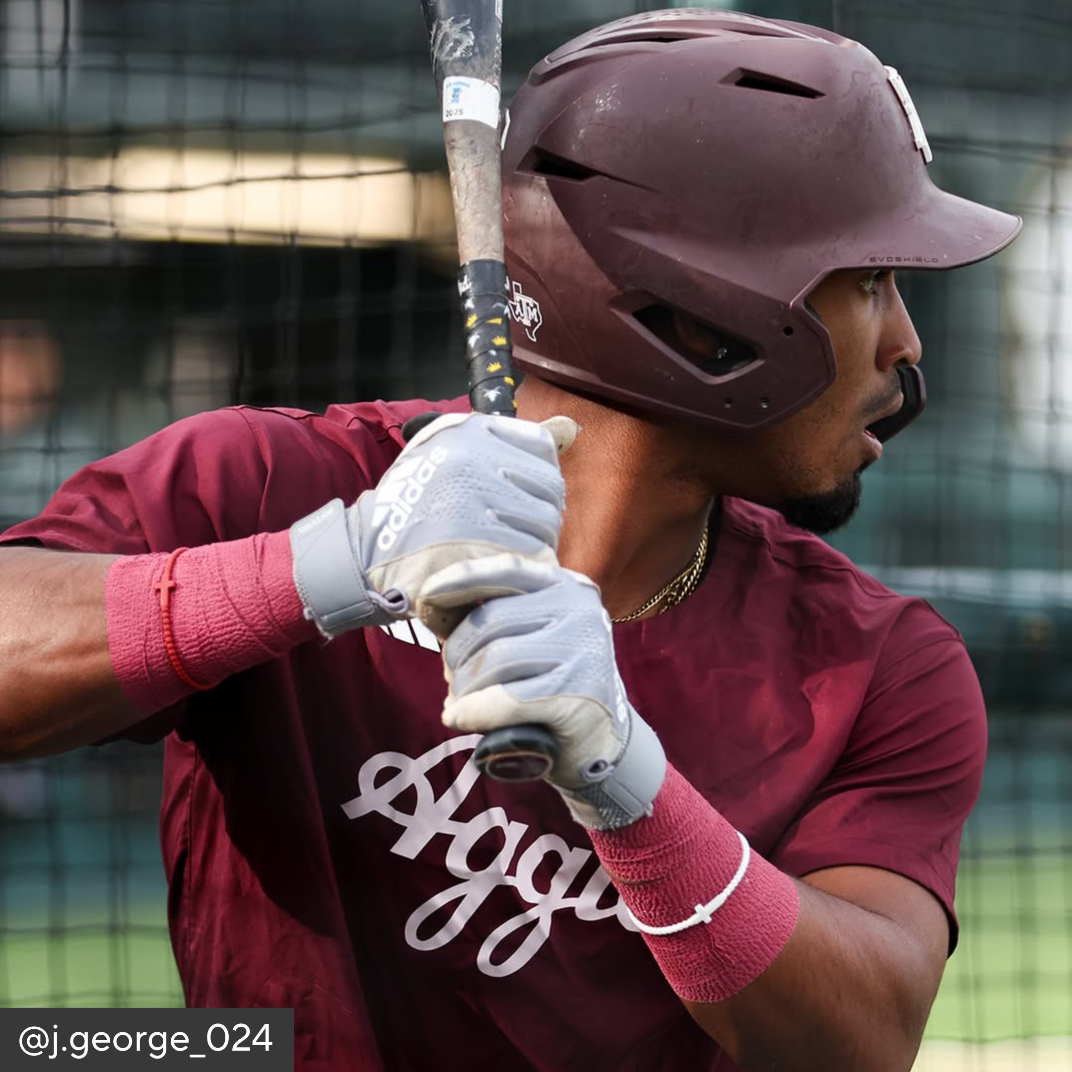 Person in maroon sports uniform with helmet and bat, wearing gloves, in a batting stance.