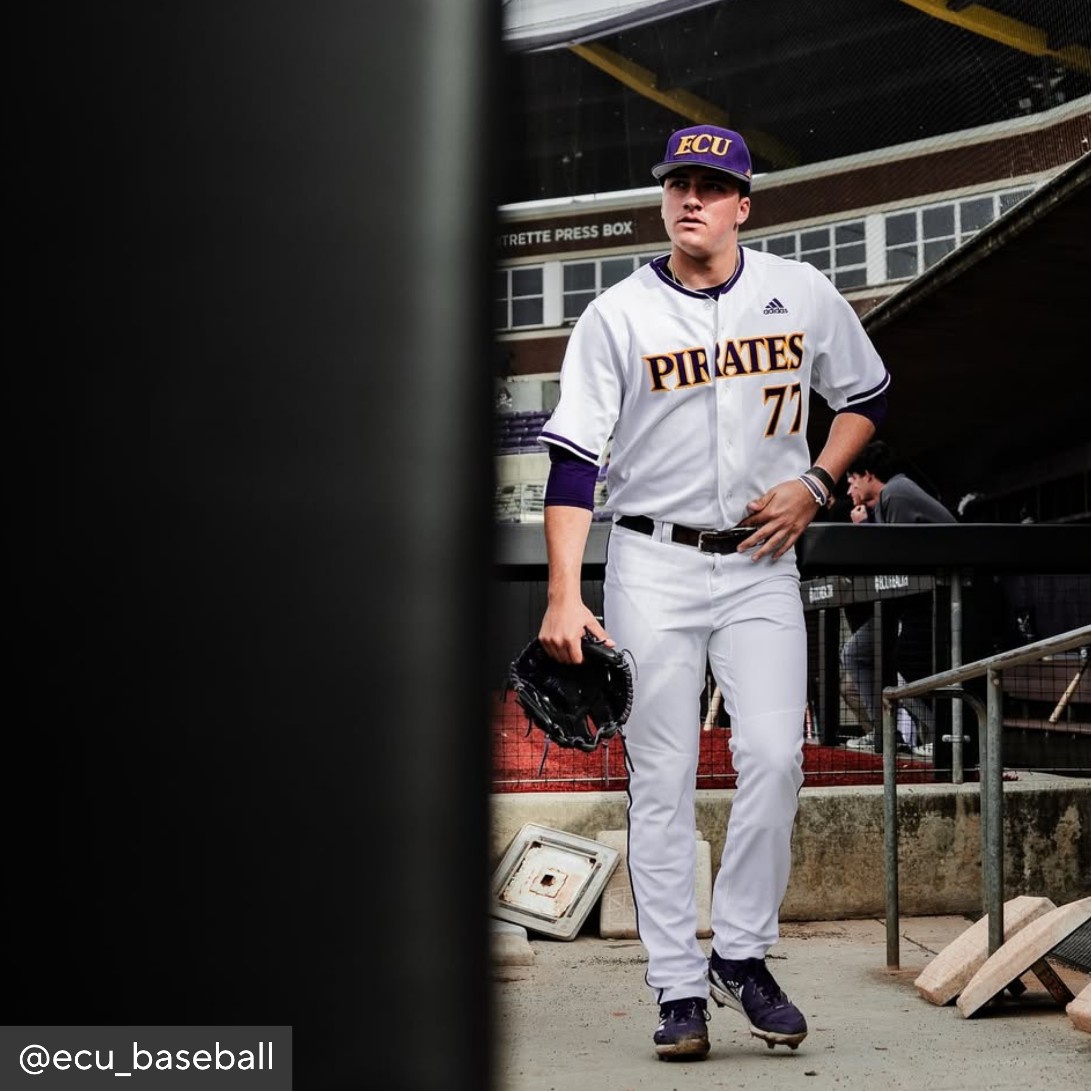 Baseball player in a Pirates uniform holding a glove in a dugout.