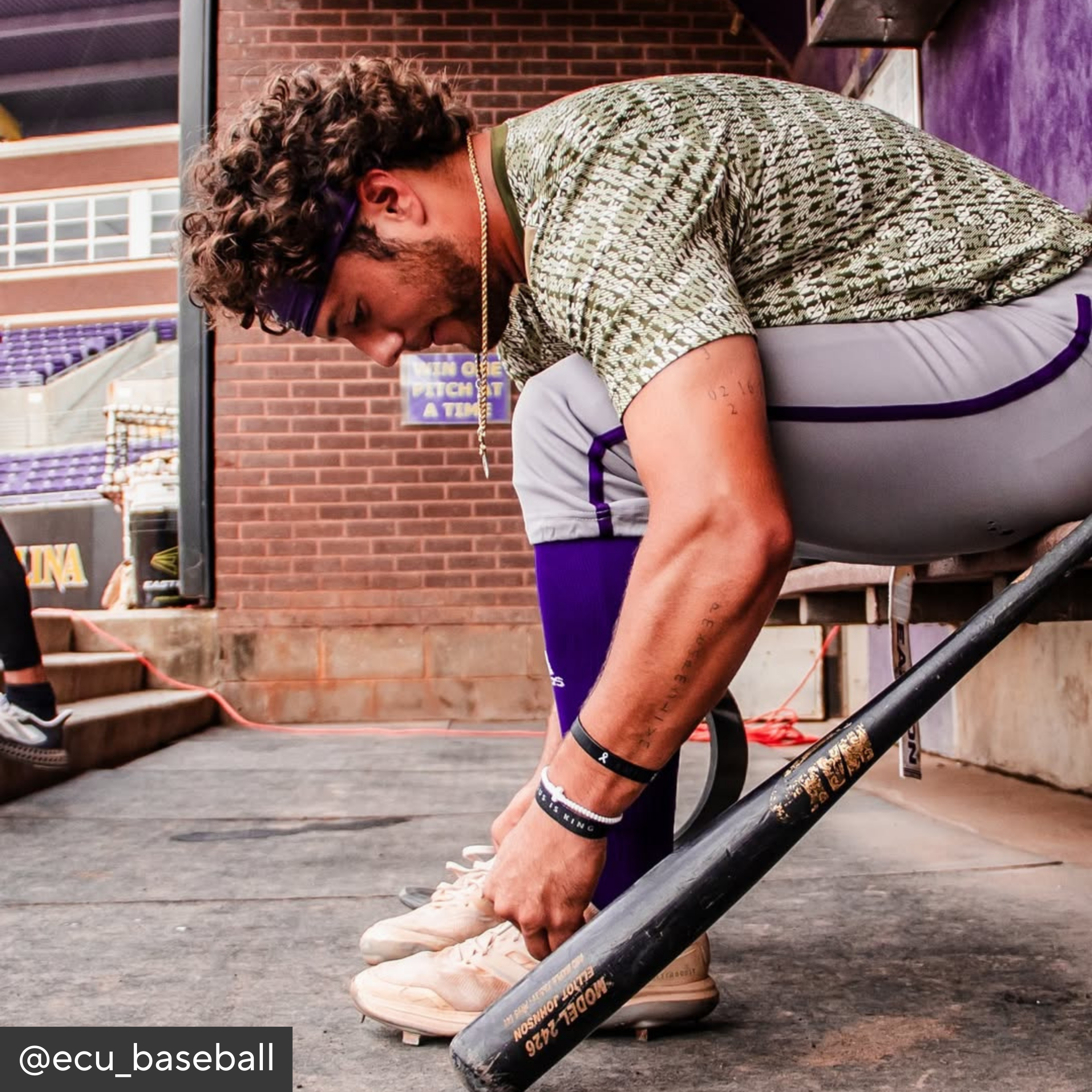 Person adjusting a baseball bat outdoors with stadium seats in the background