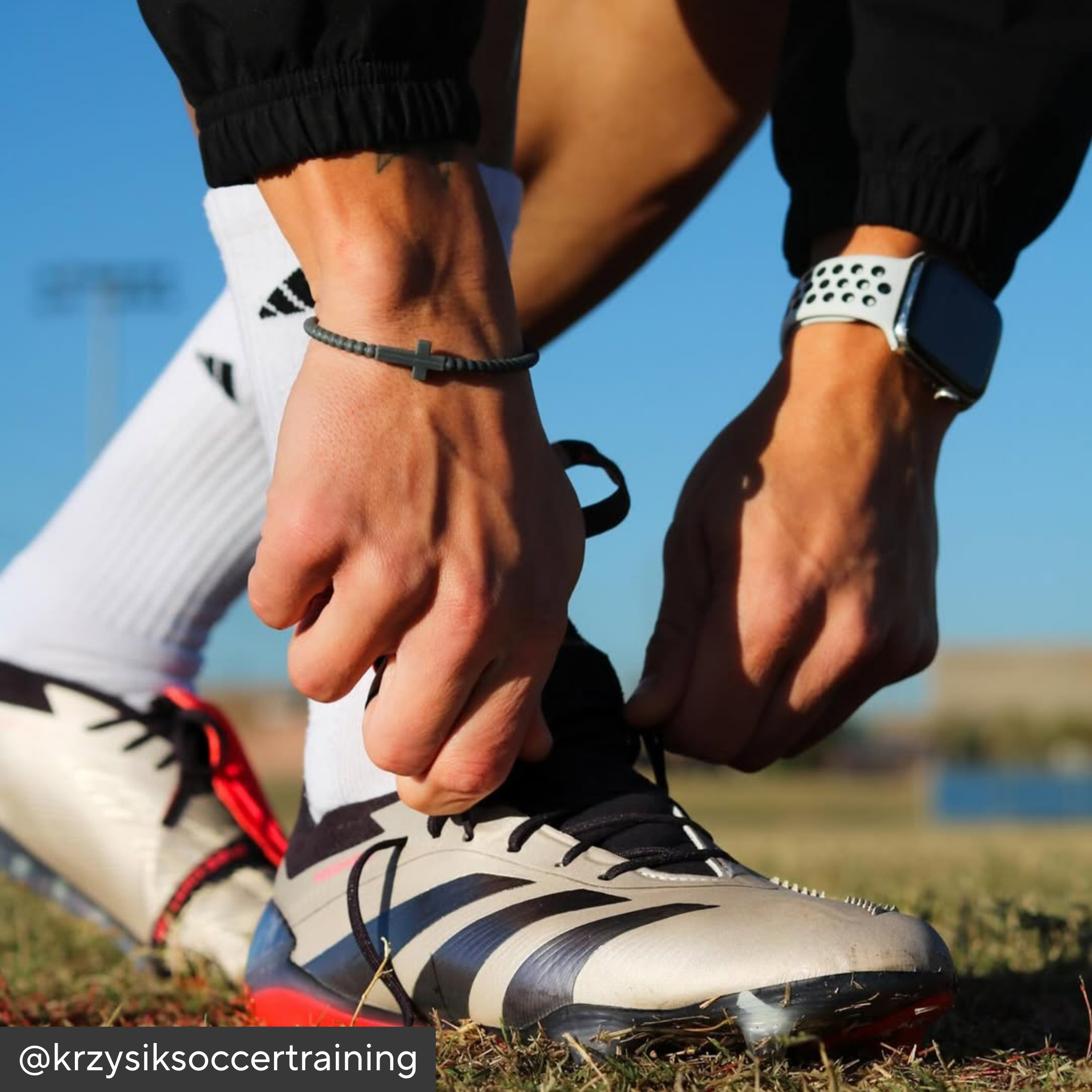 Person tying soccer cleats on a grassy field with a clear blue sky.