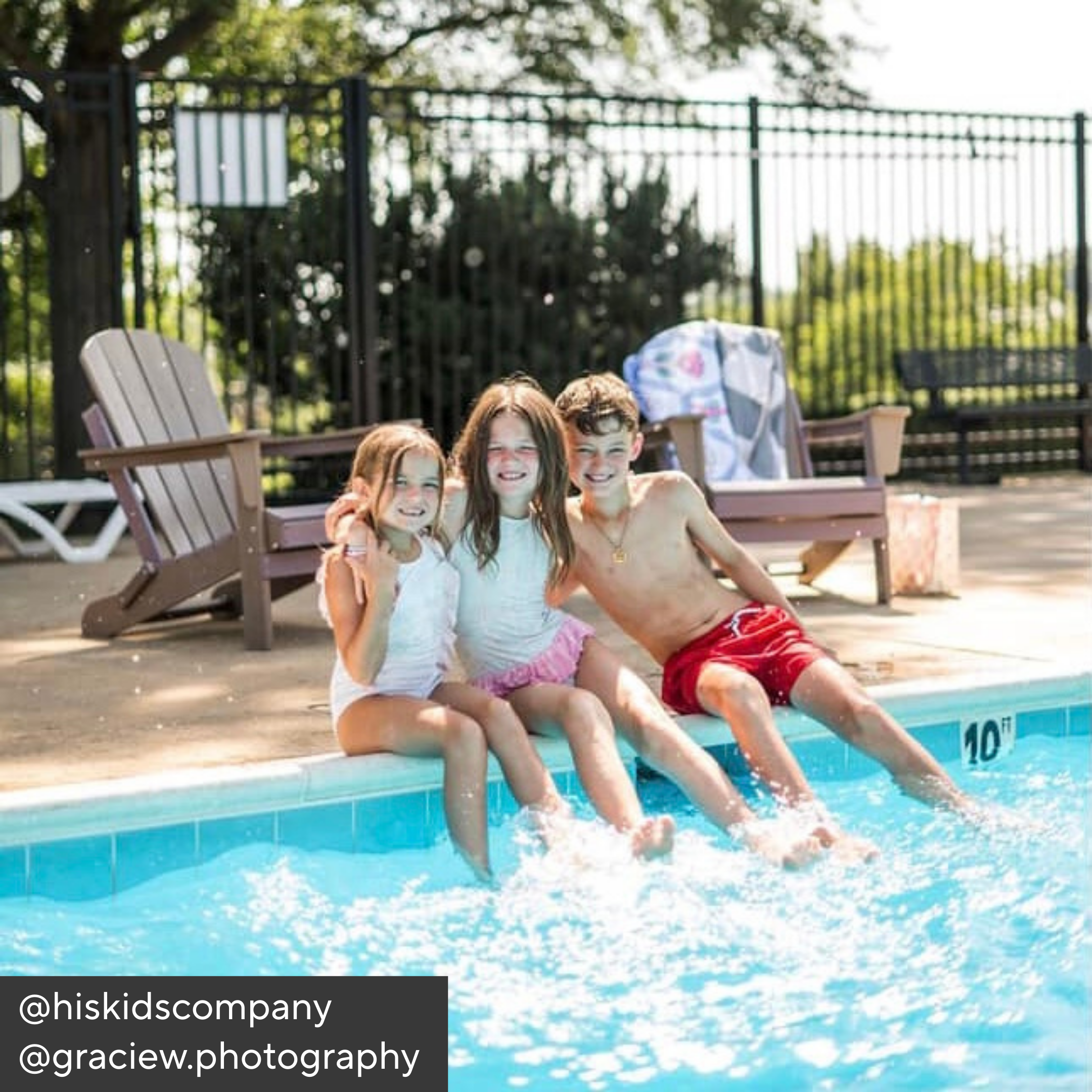 Three children sitting by a pool with chairs and a fence in the background.
