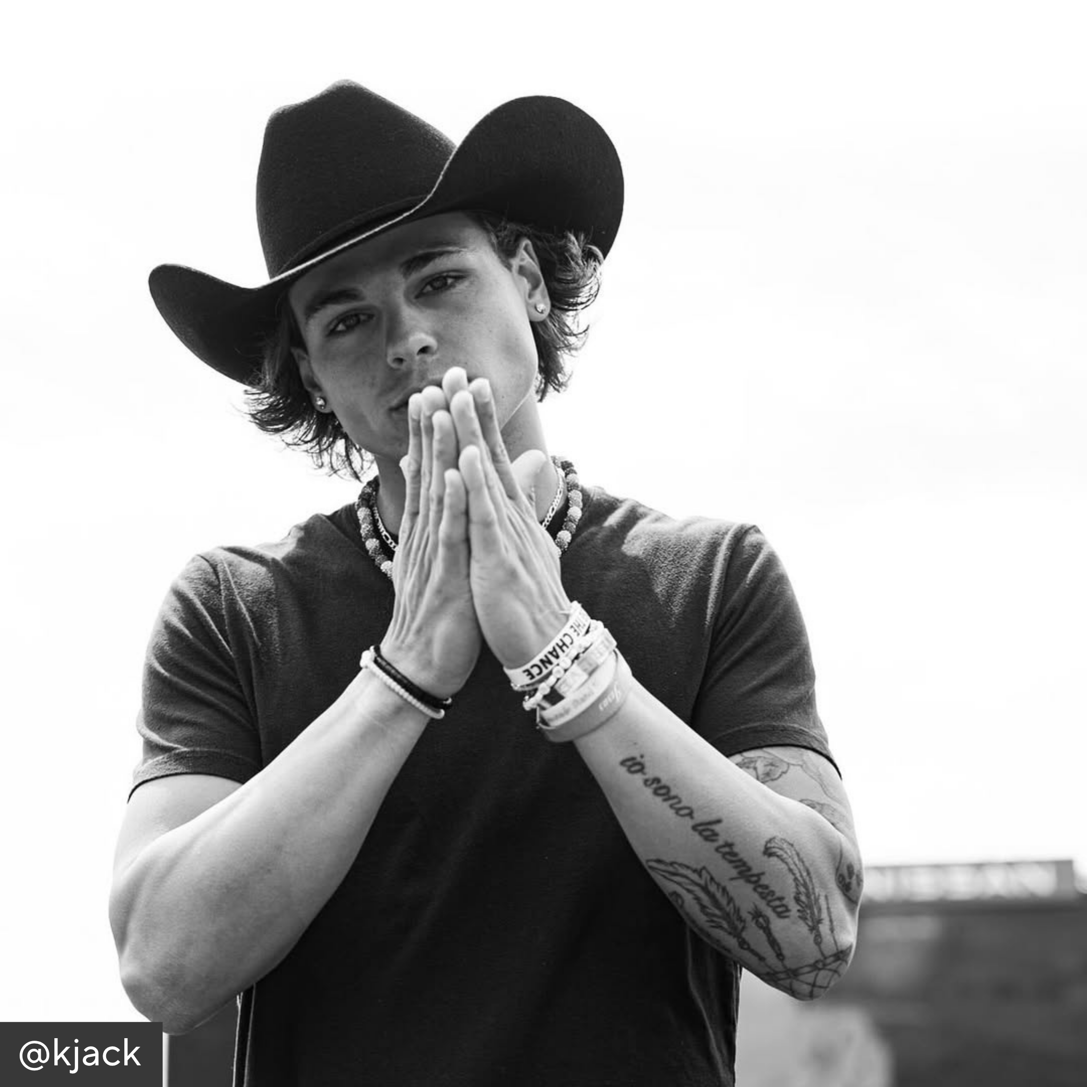 Black and white photo of a person wearing a cowboy hat with hands pressed together.
