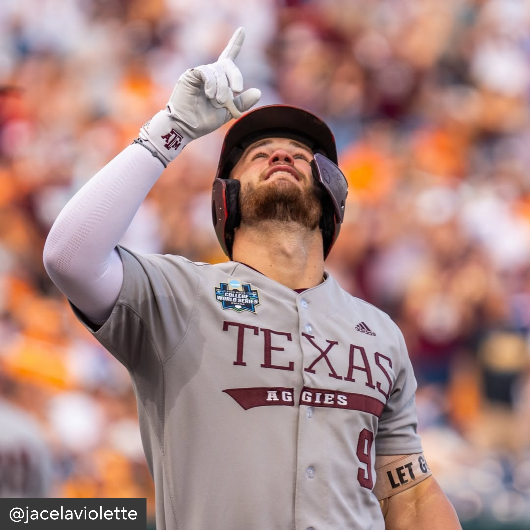 Baseball player in Texas Aggies uniform with helmet and batting glove, pointing upwards.