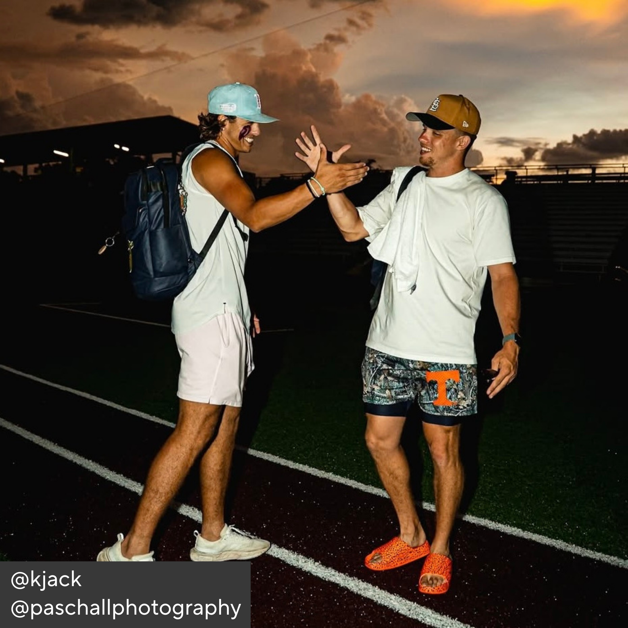 Two people high-fiving on a track field with a sunset sky.