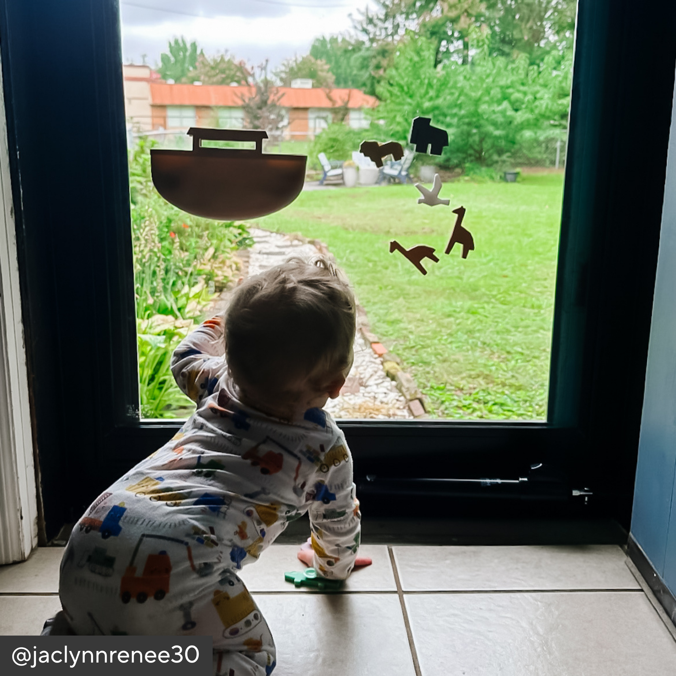 Child looking out a glass door at a garden with toys on the ground