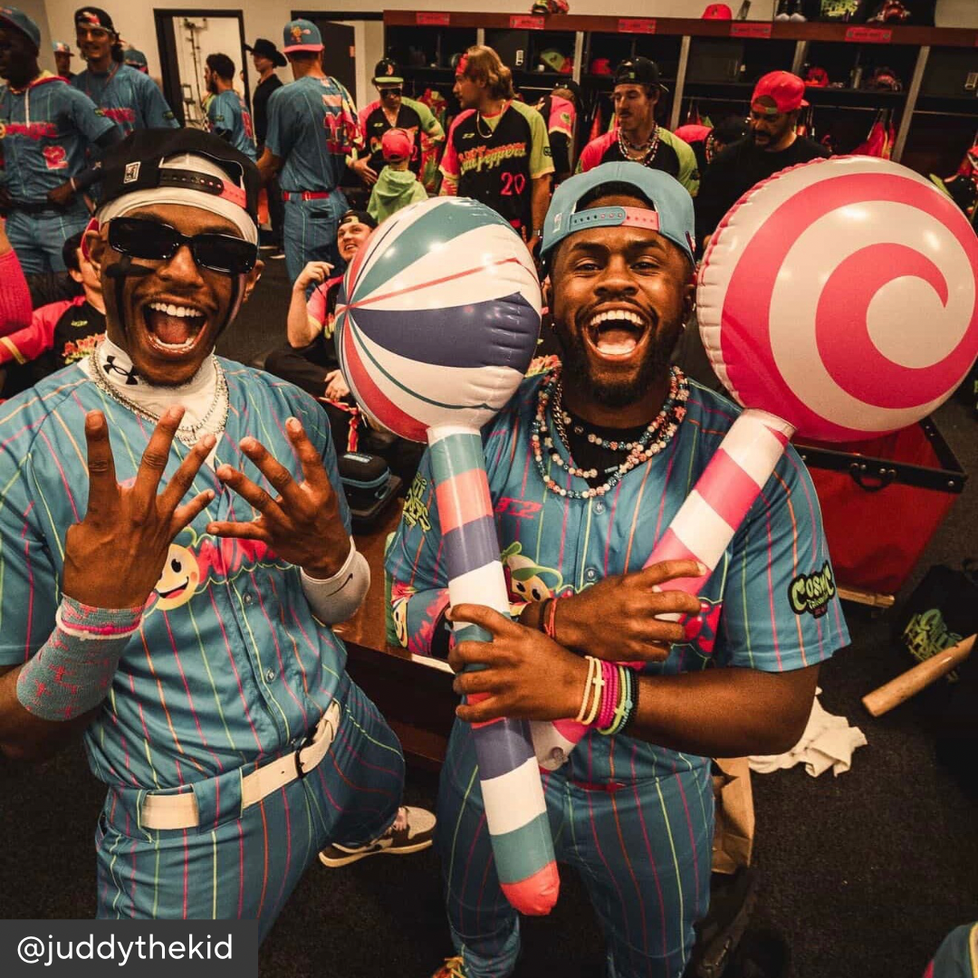 Two men in colorful outfits holding large lollipop-shaped objects in a locker room setting.