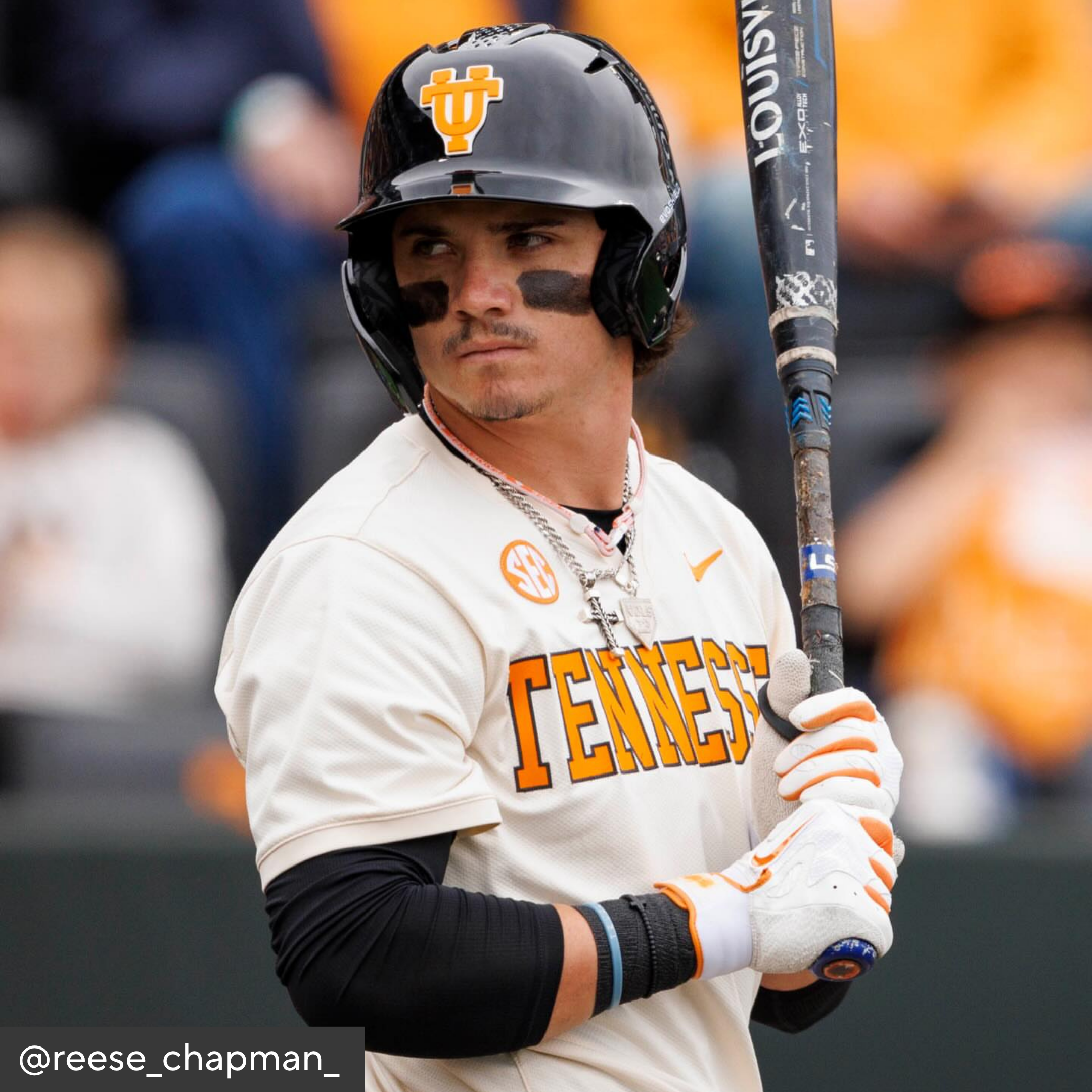 Baseball player in Tennessee uniform holding a bat with blurred spectators in the background