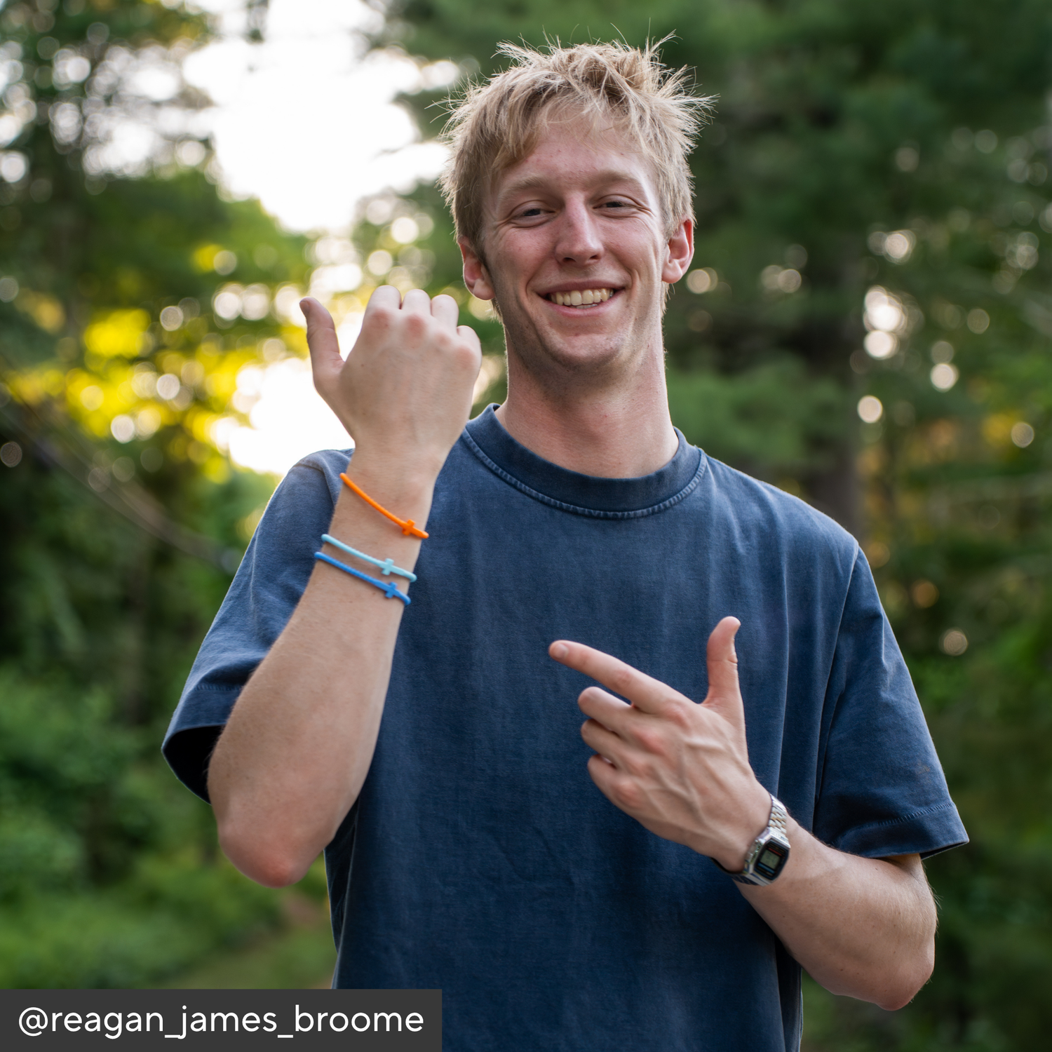 Person wearing a blue shirt with colorful bracelets, outdoors with greenery in the background