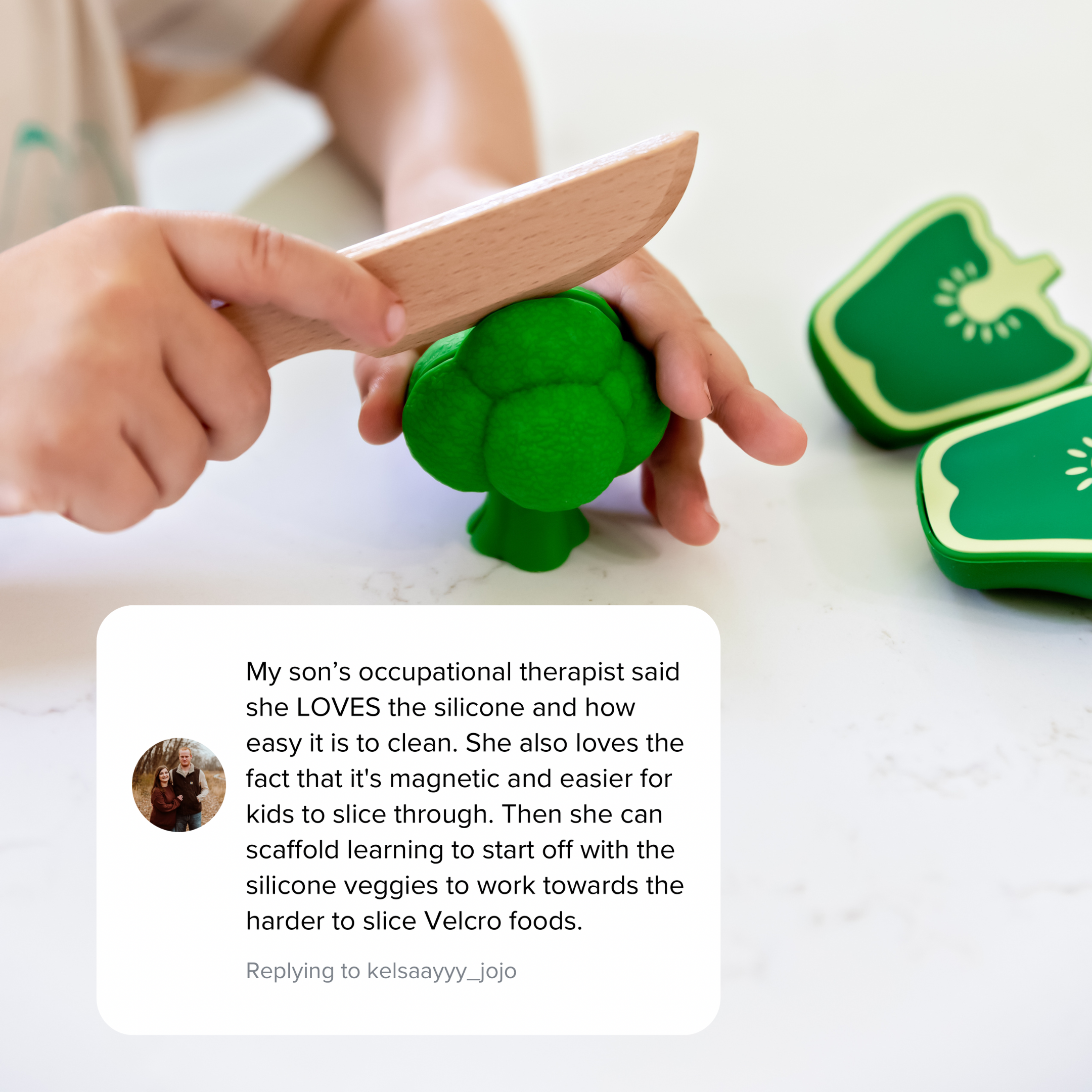 Child playing with green silicone vegetables and a wooden knife on a white surface.