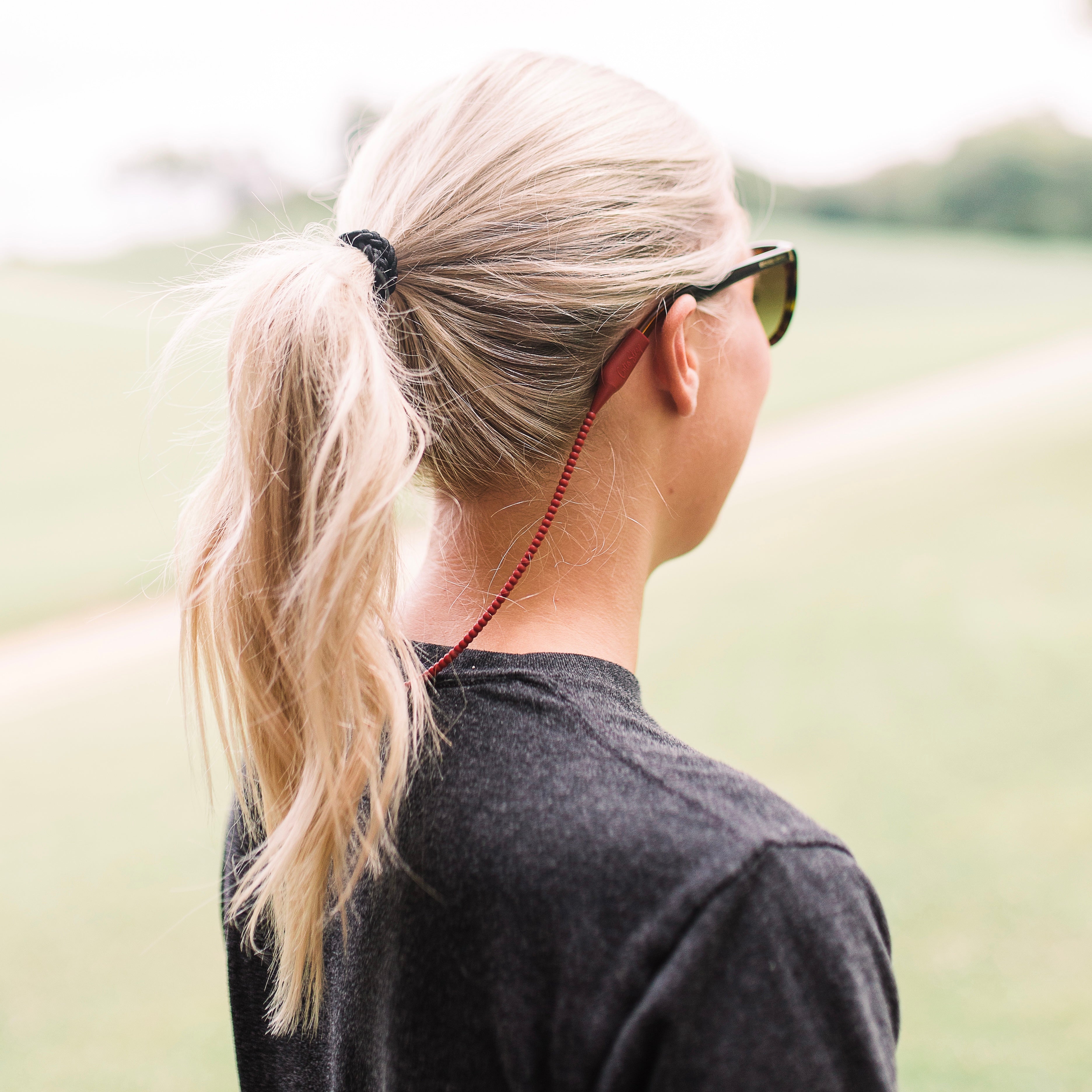 Woman wearing the Garnet Cutie Straps attached to her sunglasses.