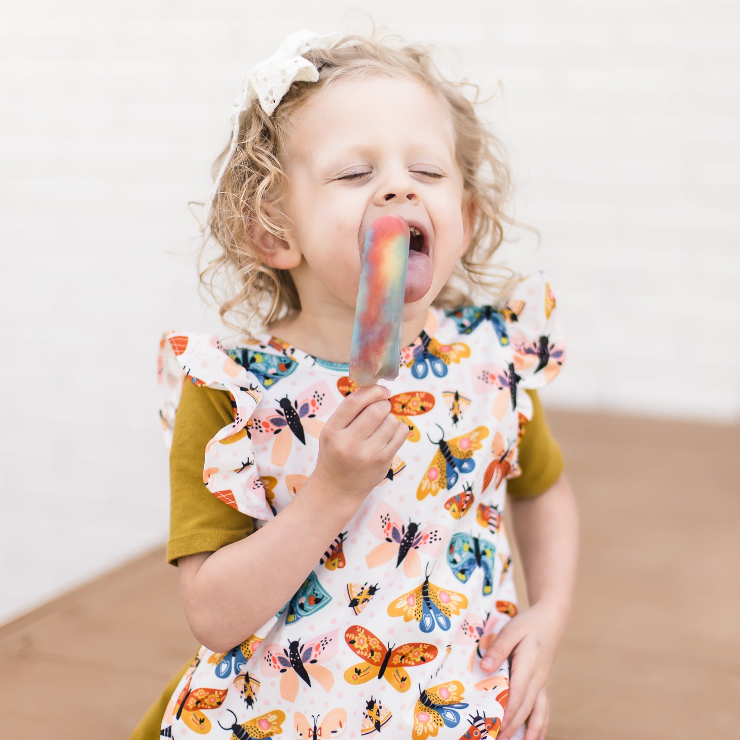 Girl eating a popsicle outside and wearing the Flutter Cutie Bapron.