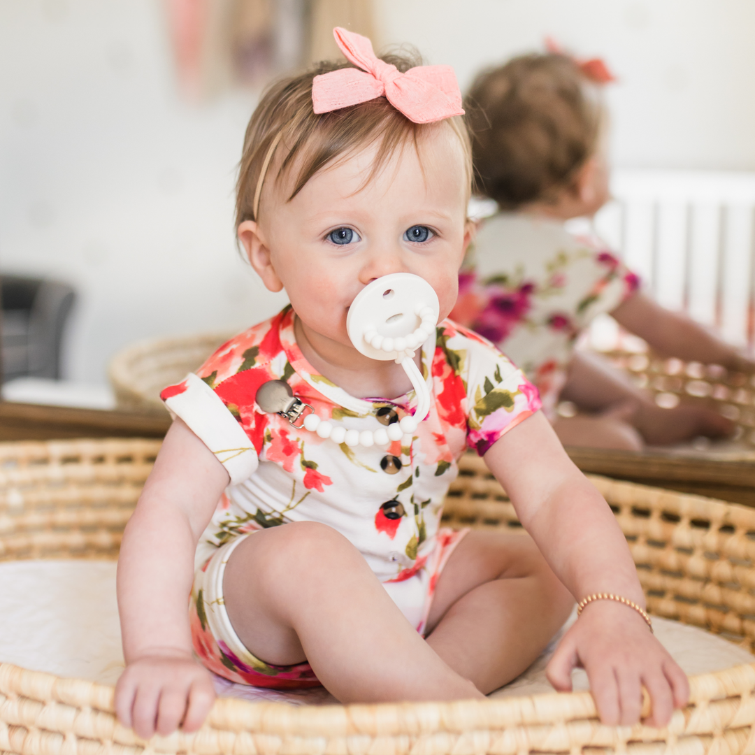 baby sitting down with a pacifier in their mouth