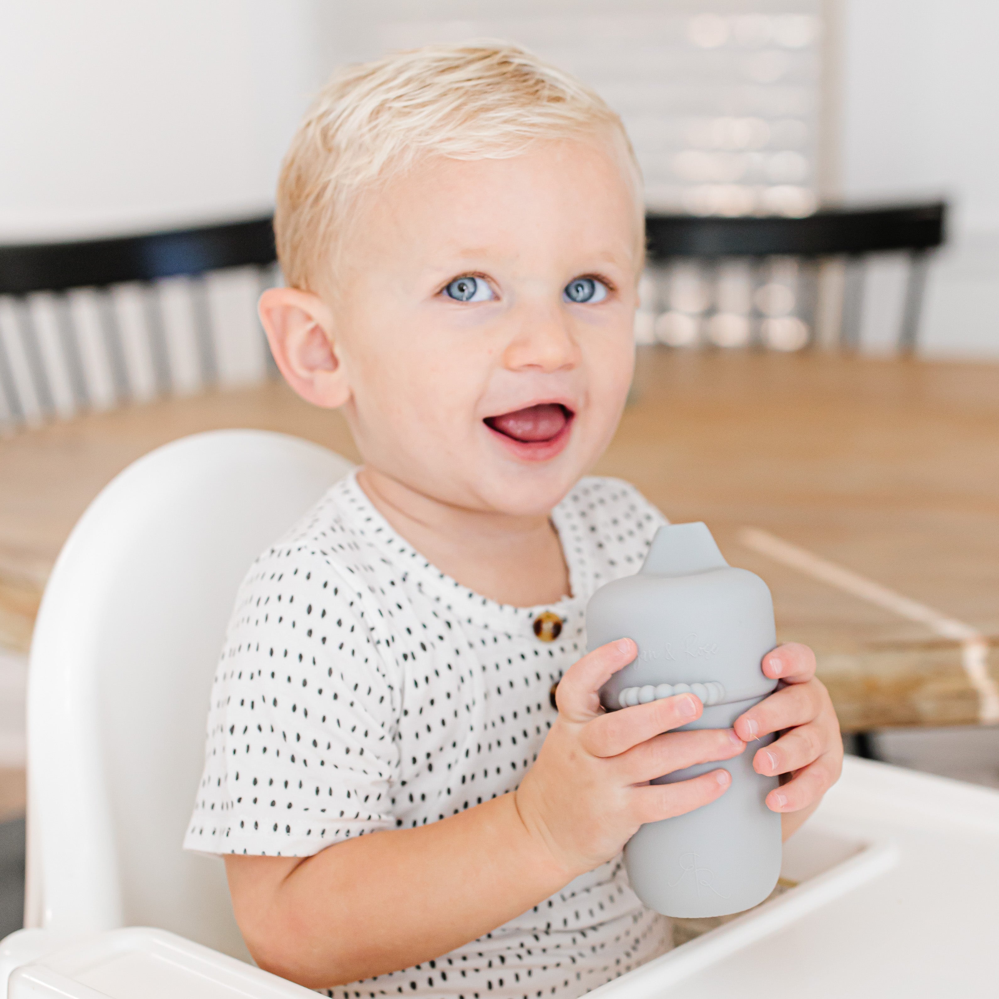 Baby sitting in high chair holding the Cutie Cup.