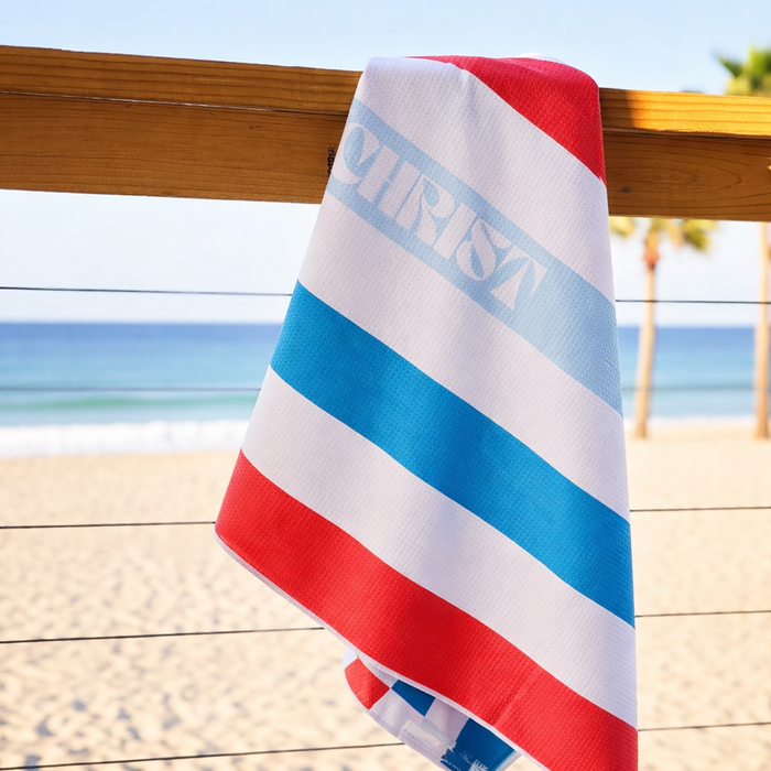 Striped beach towel with 'Christ' text on a wooden railing by the beach.