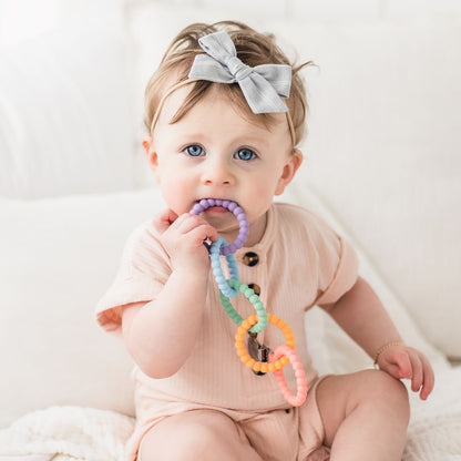 Baby girl teething on the Mosaic Cutie Clinks.