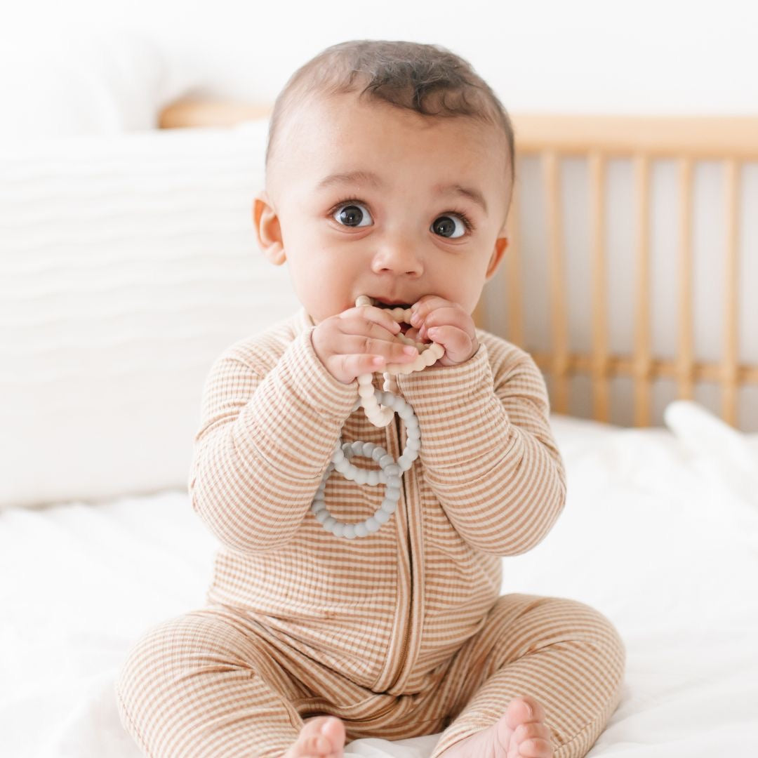 Baby boy teething on the Neutral Cutie Clinks. 