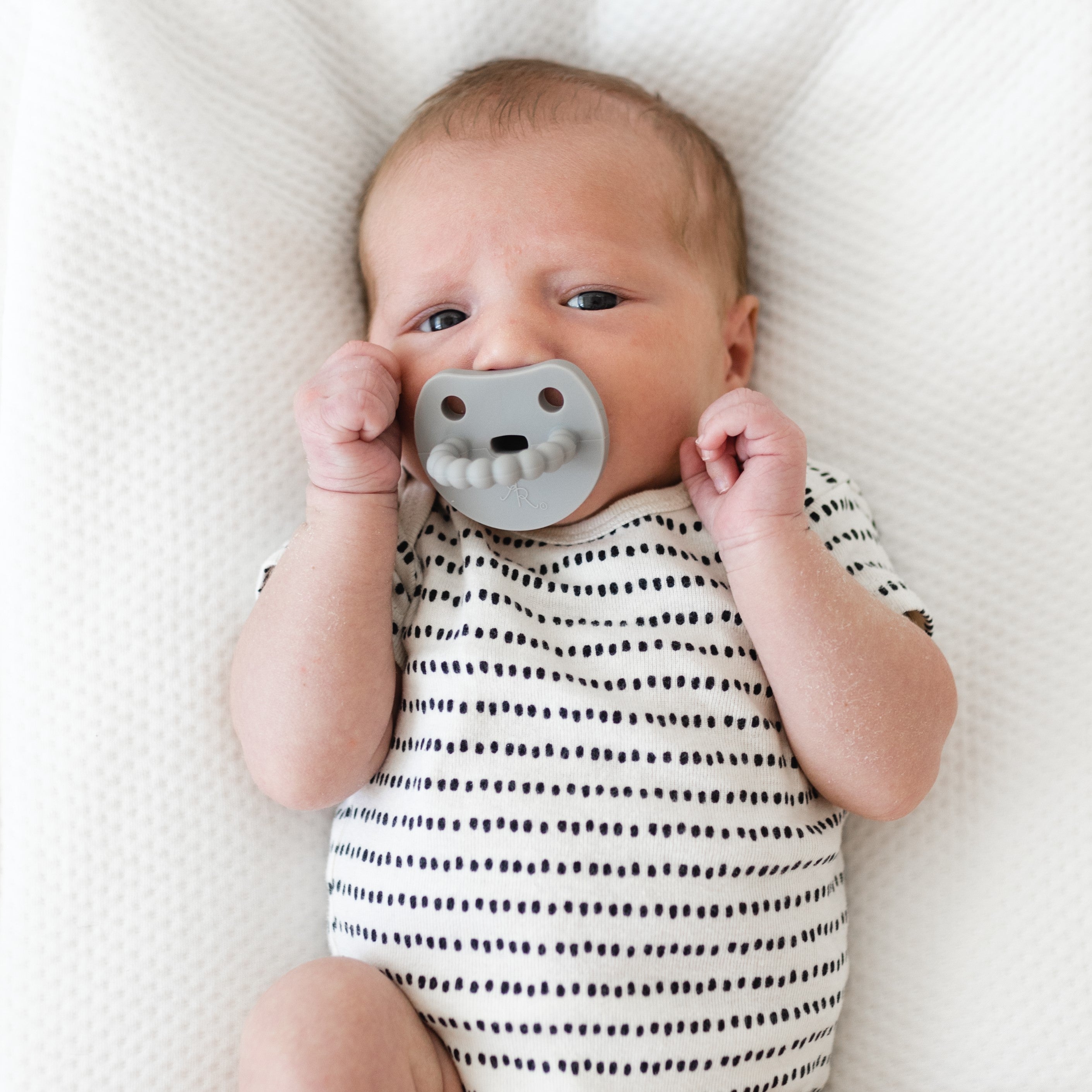 Baby sucking on a Cutie PAT Smile pacifier.