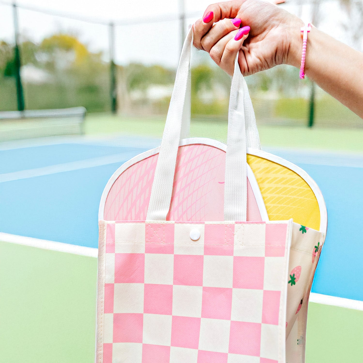 Person holding a pink and white checkered bag with a blurred background of a park.