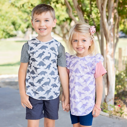 Siblings holding hands wearing the Dino Cutie Baprons in Grey and Purple.