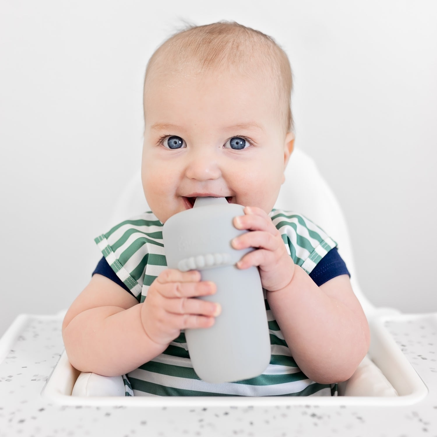 Baby sitting in high chair drinking out of the Cutie Cup.