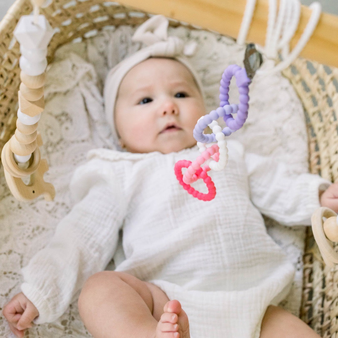 Baby girl looking at the Pixie Cutie Clinks attached to a play gym. 