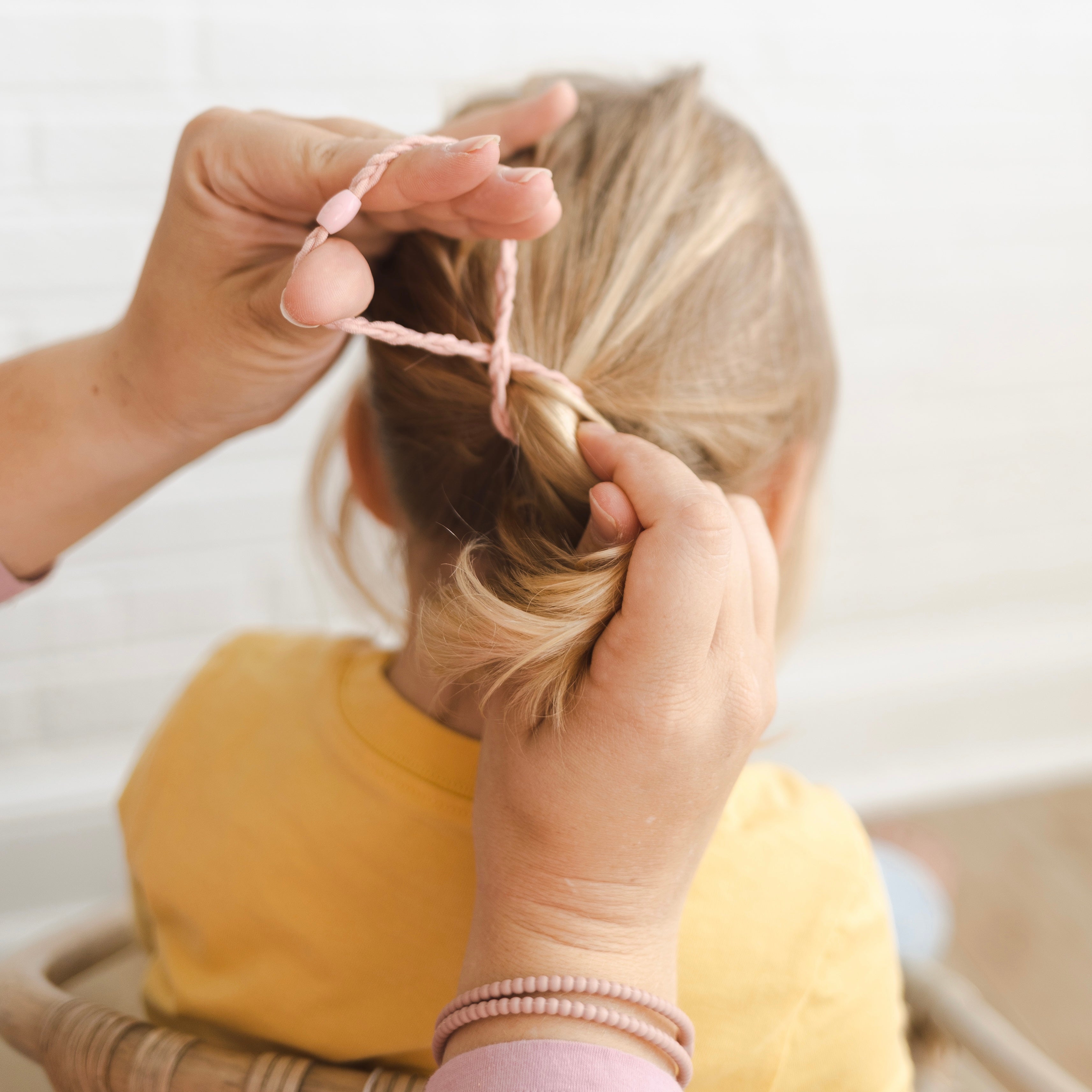Mom putting a pony tail in her daughter’s hair using a Pink Cutie Band.
