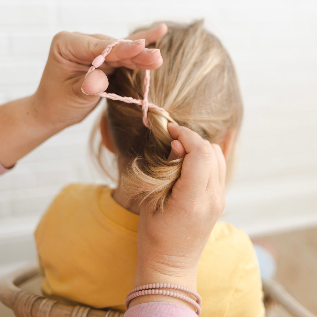 Mom putting a pony tail in her daughter’s hair using a Pink Cutie Band.