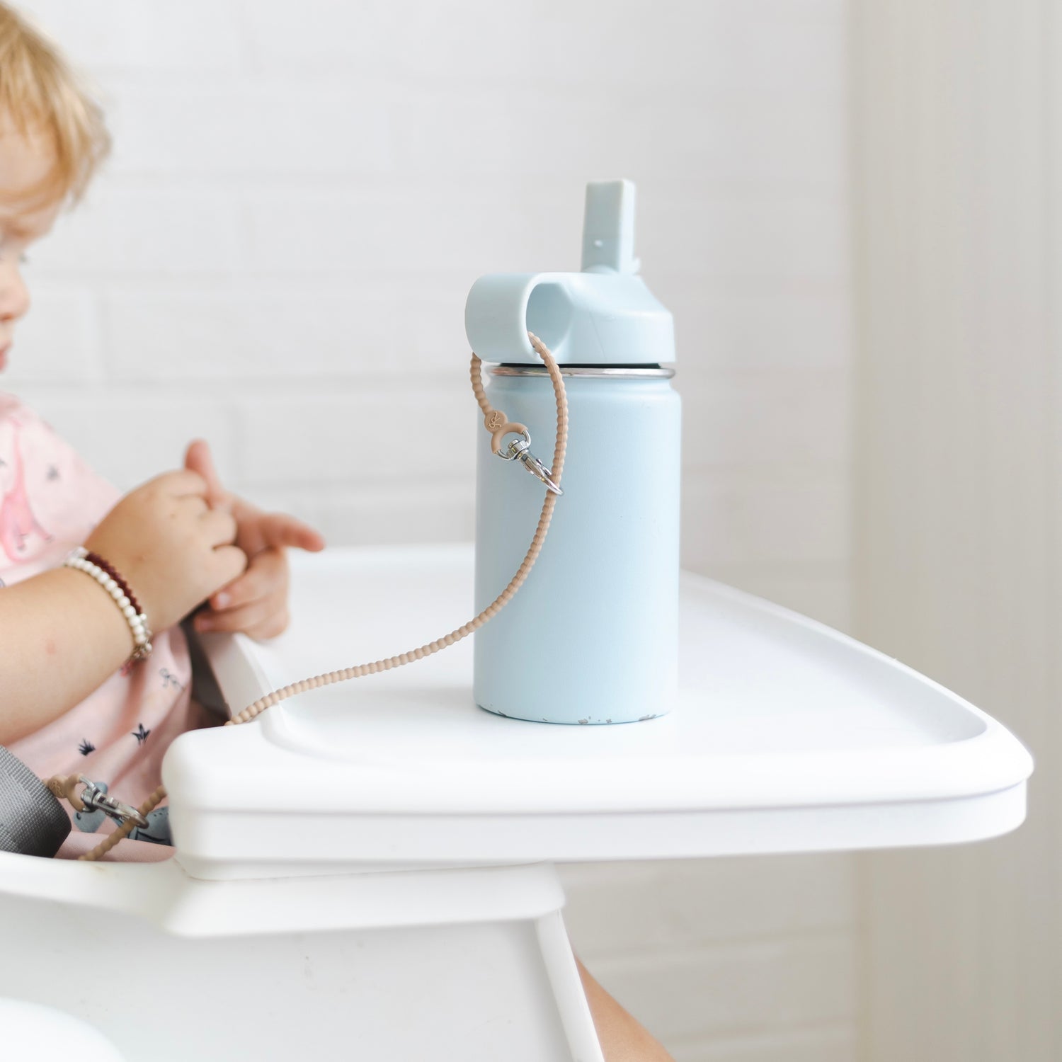 Baby sitting in a high chair with a Cutie Clasp attached to the chair and water bottle.