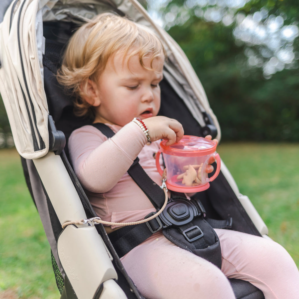 Baby sitting in a stroller with a Cutie Clasp attached to the stroller and snack container.