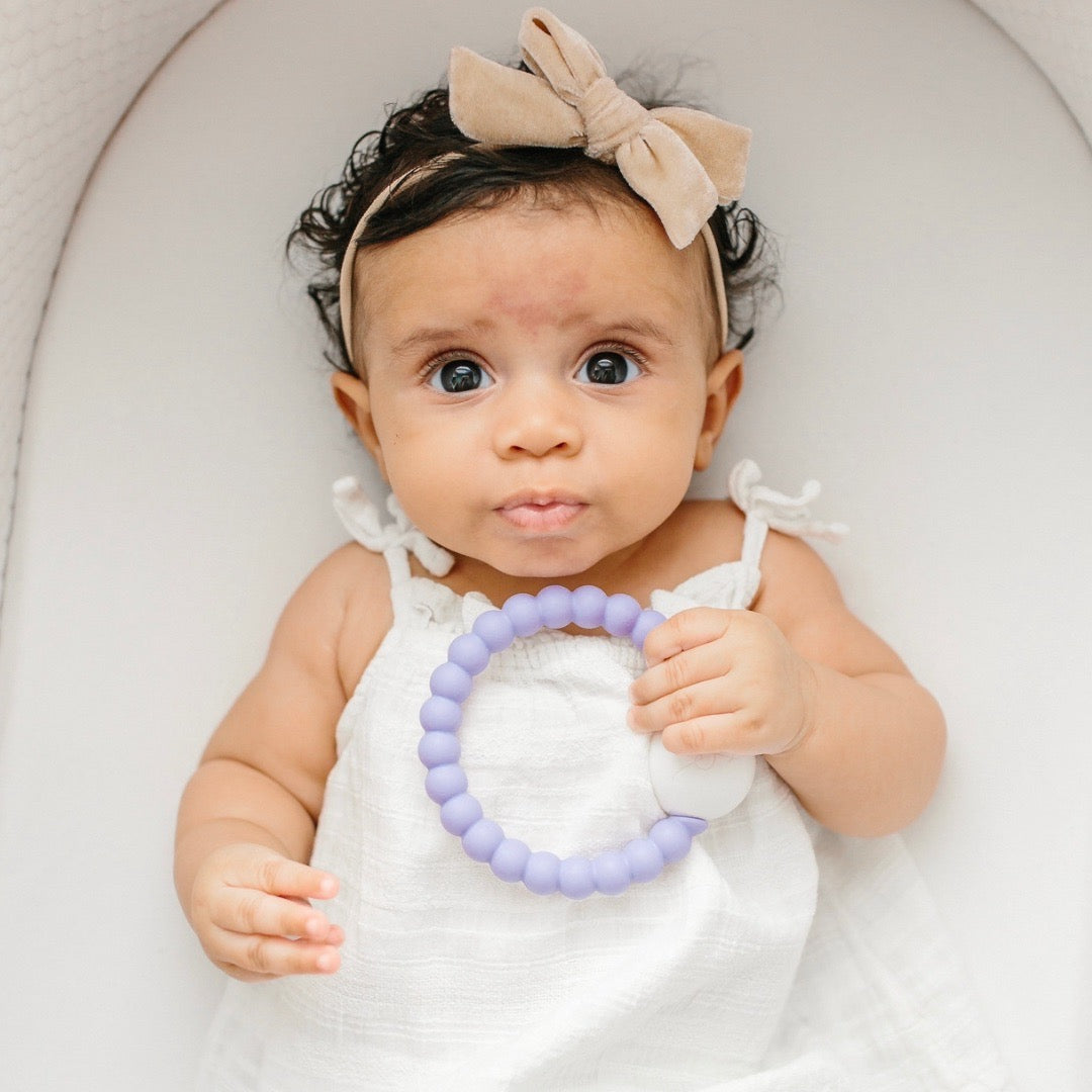 Baby girl holding the Lavender Cutie Teether.