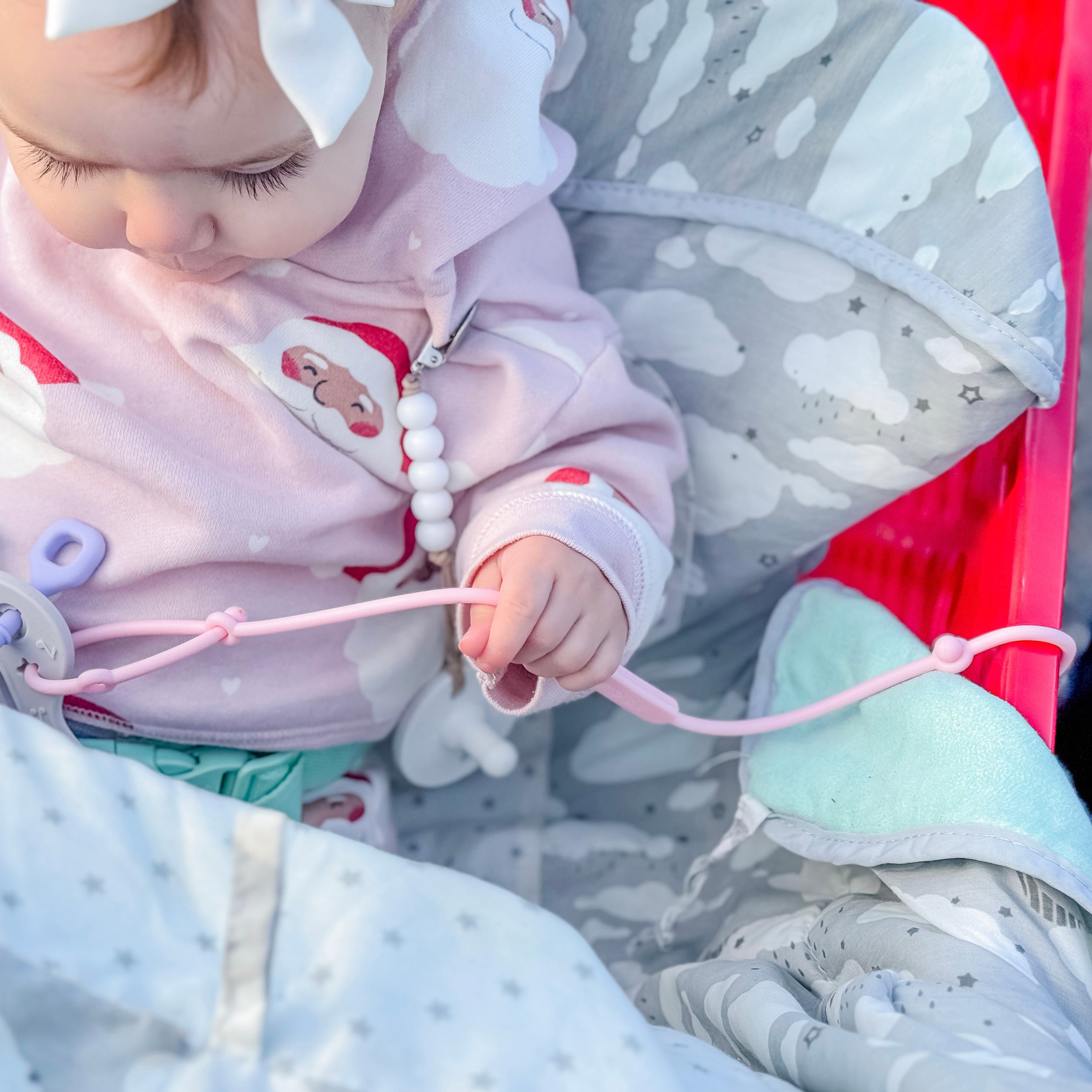Baby in a pink outfit with a white bow, sitting on a red chair.
