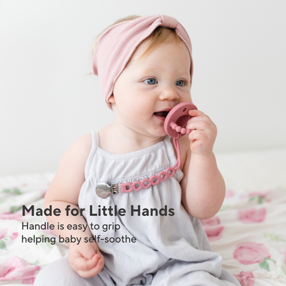 Baby wearing a pink headband and holding a pink teething ring with text &