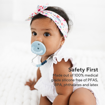 Baby wearing a floral headband and blue pacifier with text about product safety and material composition.
