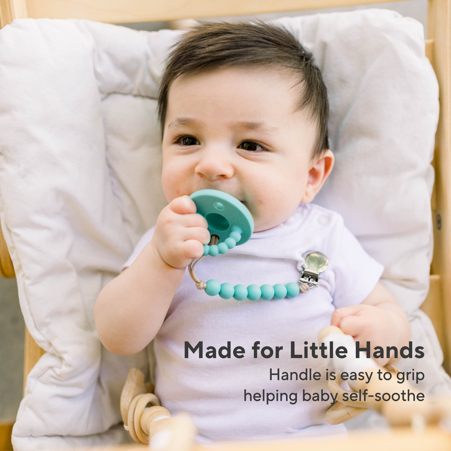 Baby holding a turquoise teething ring with text &