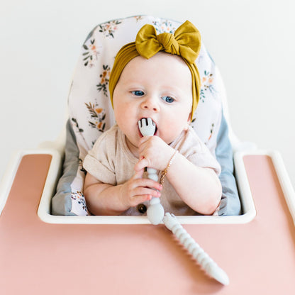 Baby sitting in high chair using Cutie Tensils.