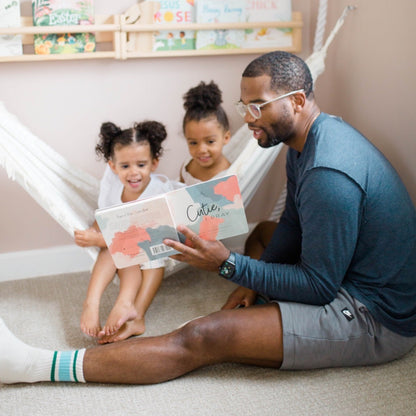 A dad reading Cutie, I Pray to his daughters.