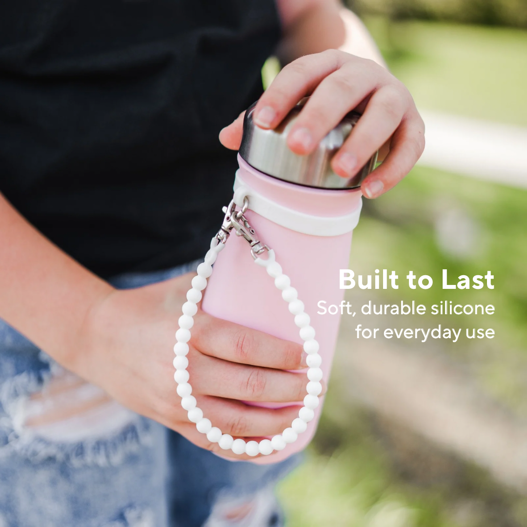 Person holding a pink silicone water bottle with a beaded strap, outdoors.