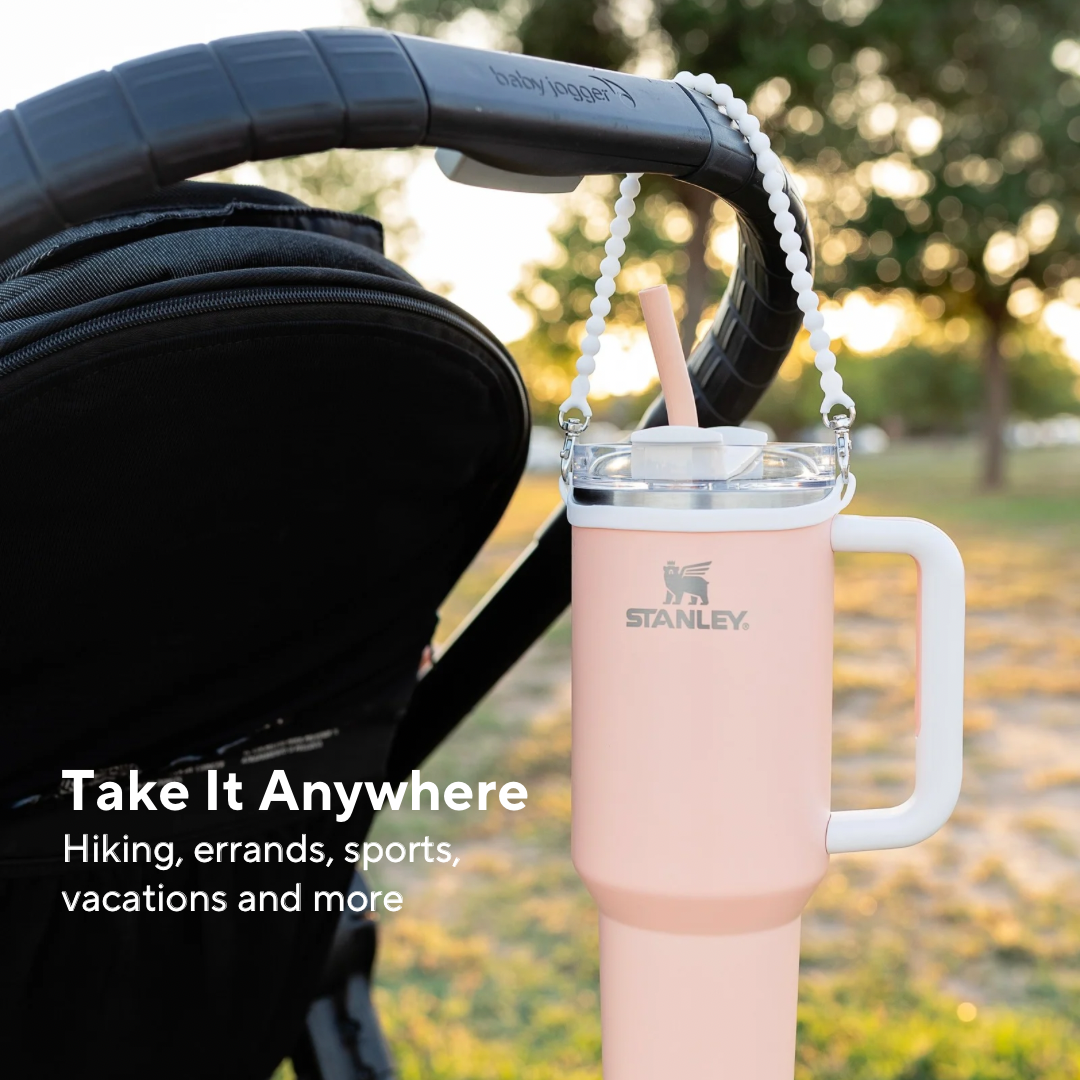 Stanley pink water bottle with handle attached to a stroller in an outdoor setting