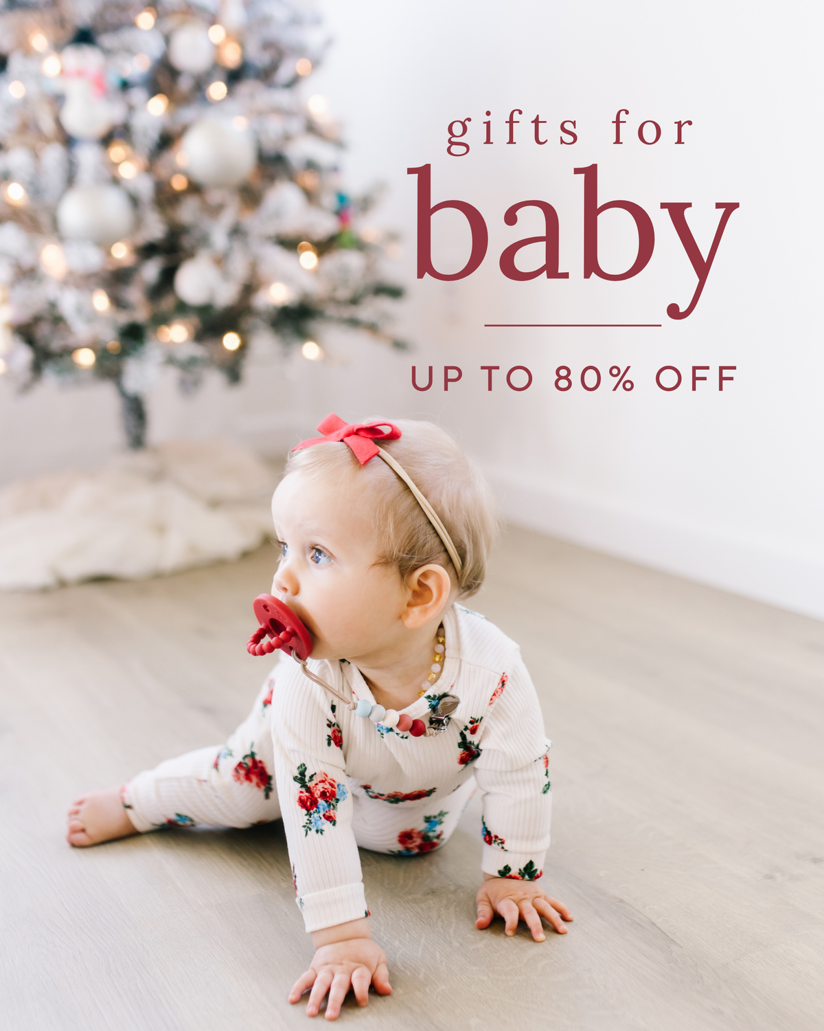 Baby with a pacifier sitting in front of a Christmas tree on a baby sale promotion banner
