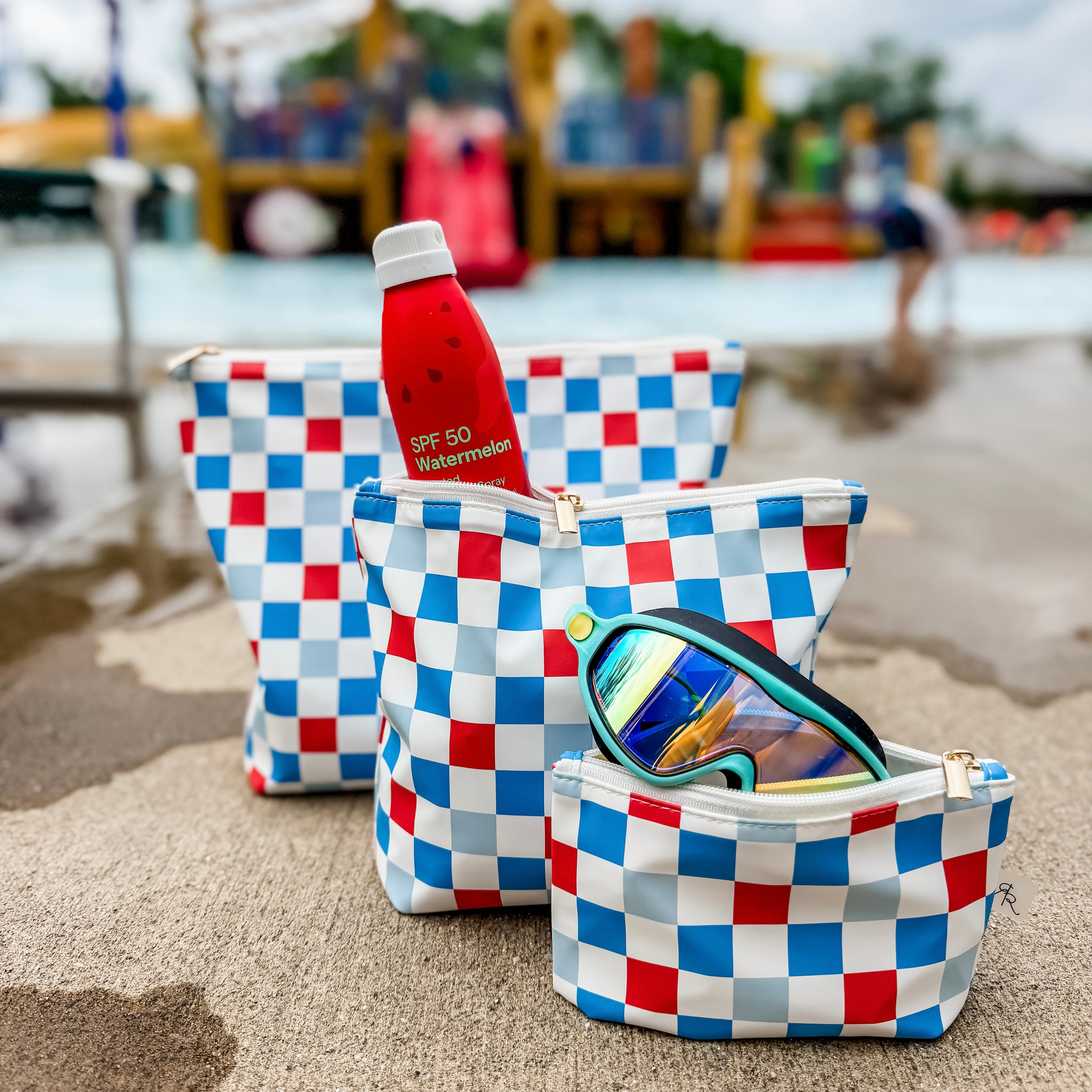 Set of three checkered pouches with a water bottle and sunglasses on a beach.