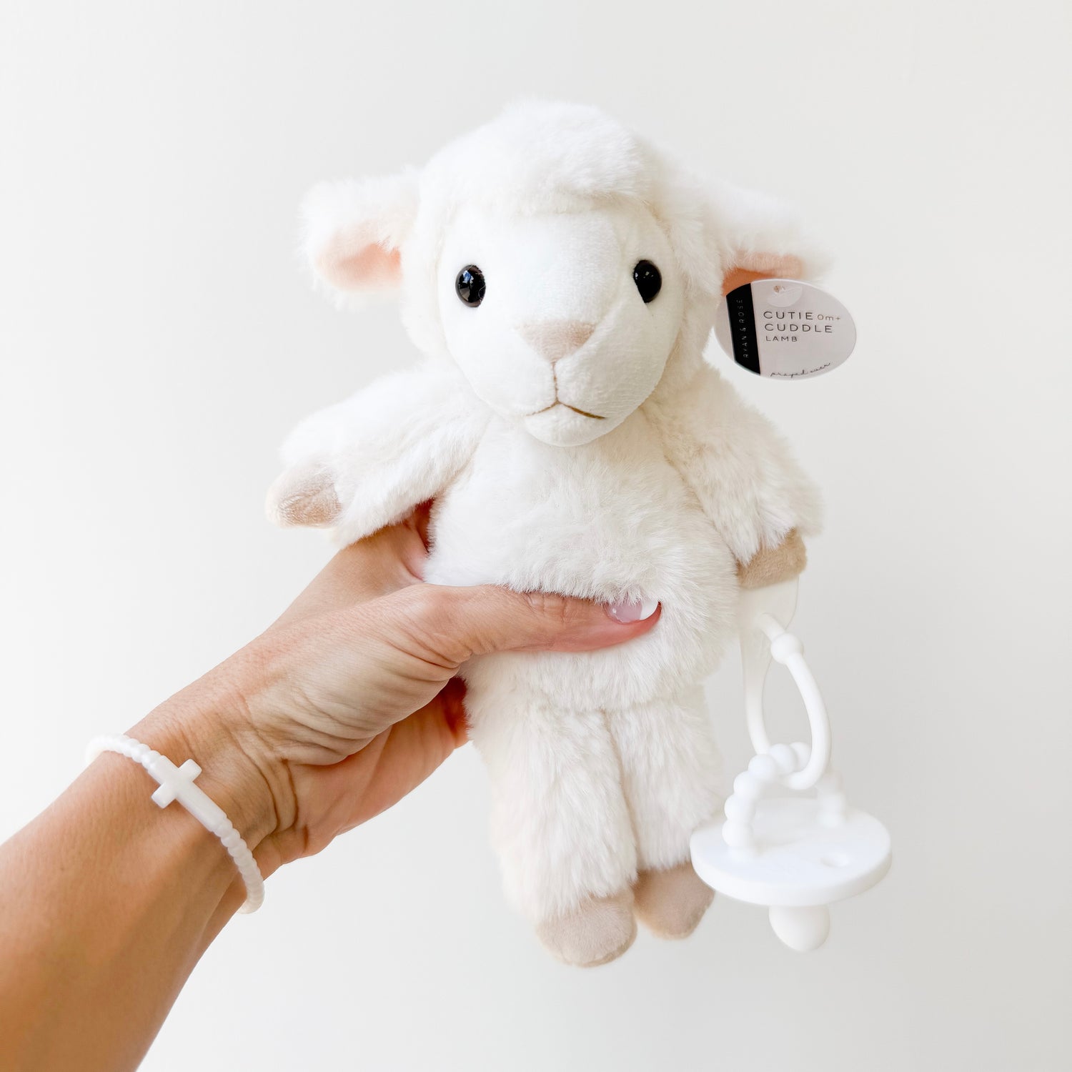 White plush lamb toy held in a hand against a white background
