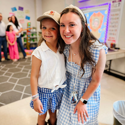 Two young girls posing together in a classroom setting with educational posters on the wall.