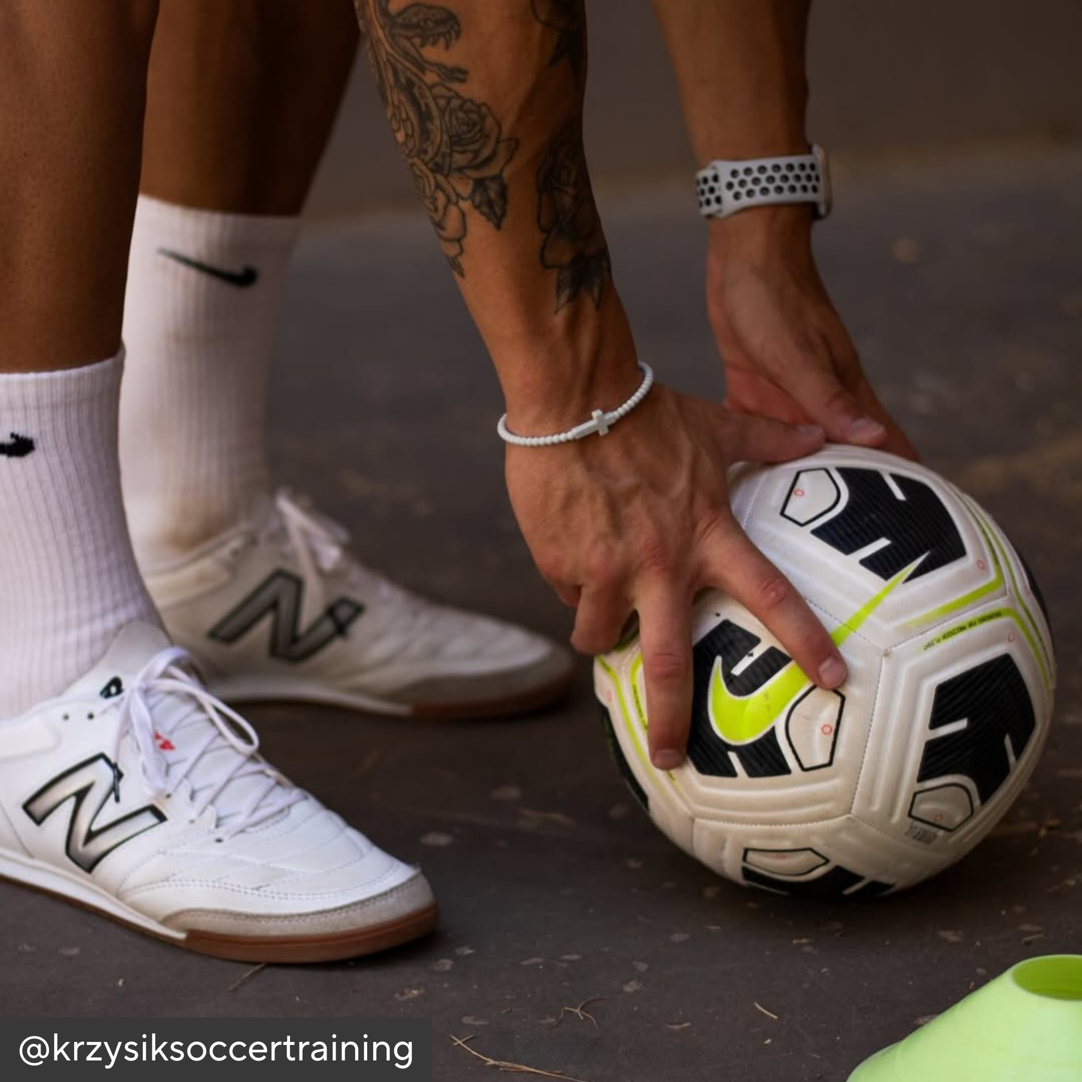 Person holding a soccer ball with sports shoes and socks in the background