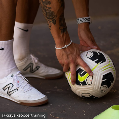 Person holding a soccer ball with sports shoes and socks in the background