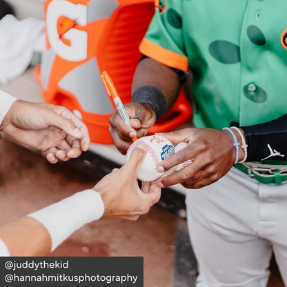 Person in sports uniform holding a baseball with another person, with a focus on the interaction.